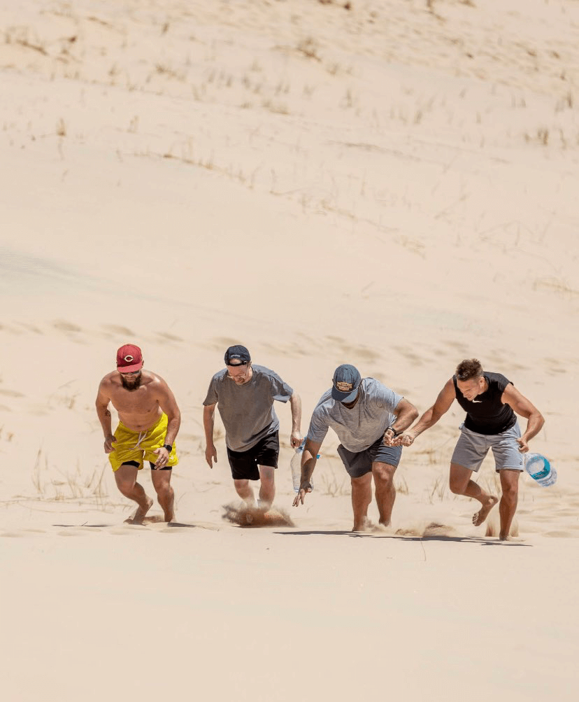 4 men running up a sand dune